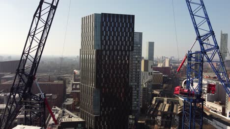 Luftdrohnenflug-Zwischen-Zwei-Baukränen-Auf-Der-Oxford-Road-In-Manchester-City-Und-über-Und-über-Einem-Turmdach,-Um-Eine-Skyline-Der-Südtürme-In-Der-Ferne-Zu-Enthüllen