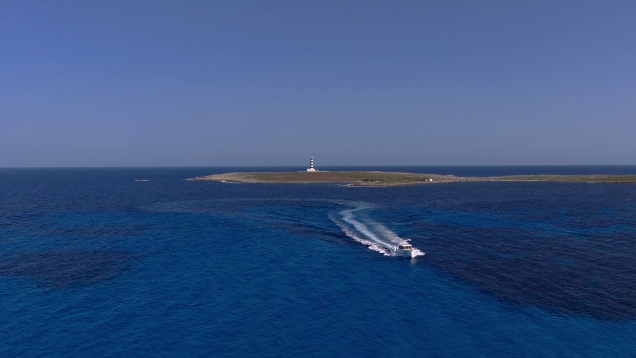 Drone Panorama of Menorca’s Illa de l’Aire Lighthouse on Islet with motorboat sailing Mediterranean sea