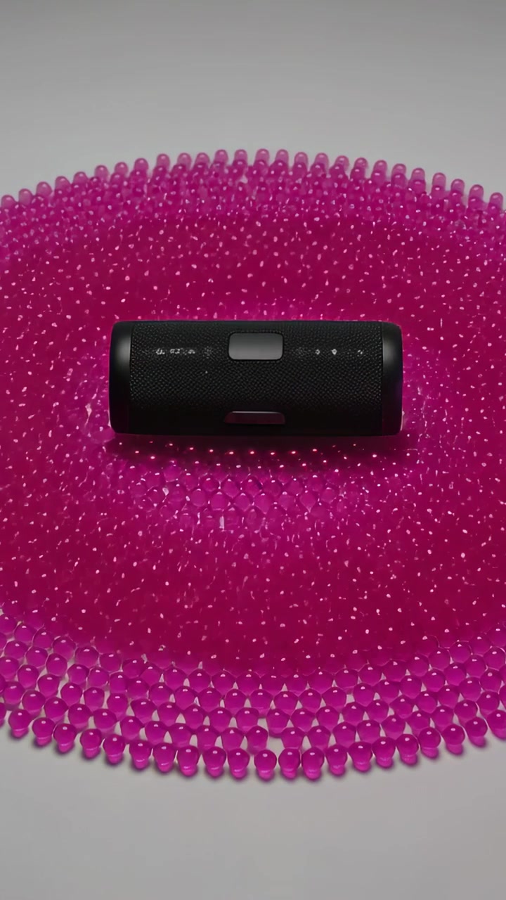 Video verticale: Altoparlante nero vibrante che emette bassi, che deforma un tappetino di perline magenta su un tavolo bianco