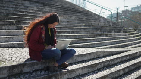 thoughtful beautiful woman sitting on stairs with laptop on knees