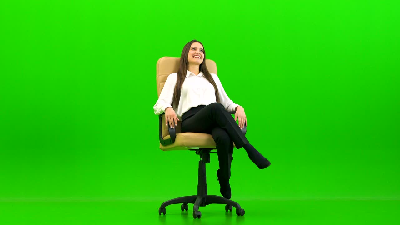 The businesswoman sitting on the office chair and laughing on a green background