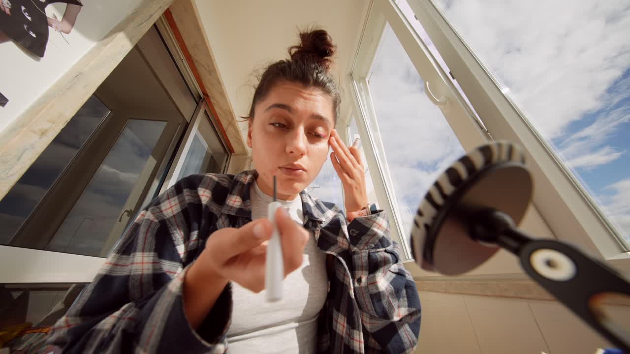 Giovane donna che applica l'eyeliner e parla alla telecamera per un vlog di bellezza.