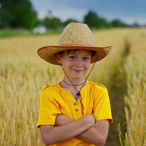 boy in yellow t-shirt on field with spikelets. portrait of a little farmer in hat among agriculture in the countryside.