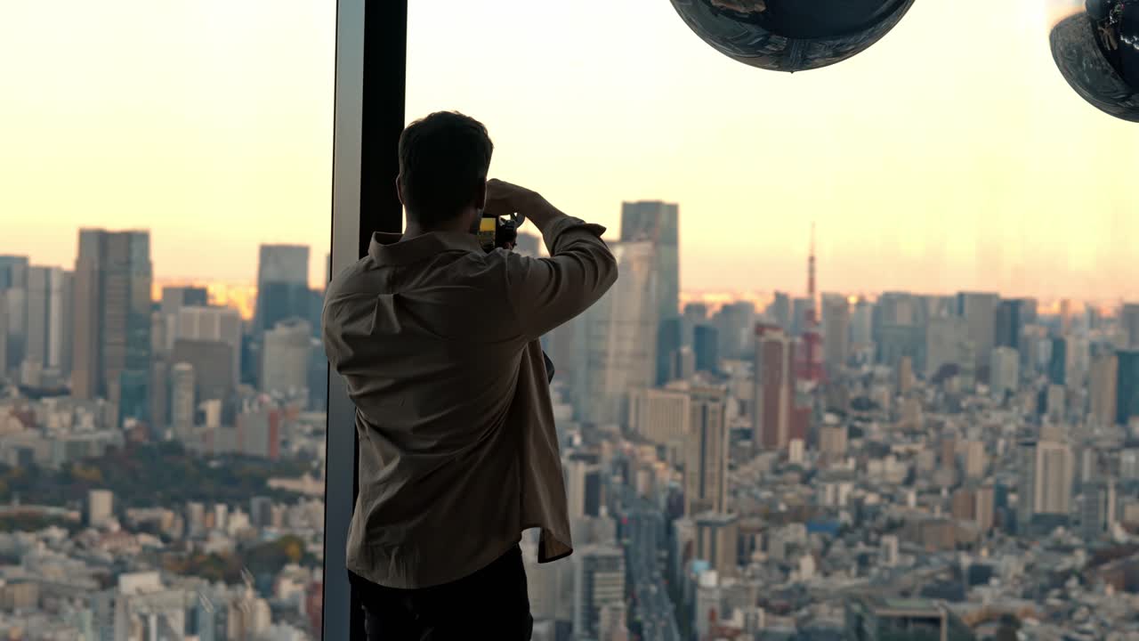 A cinematic shot of a man photographing the stunning view of Tokyo Tower and the cityscape at sunset from the window at Shibuya Sky, Tokyo.