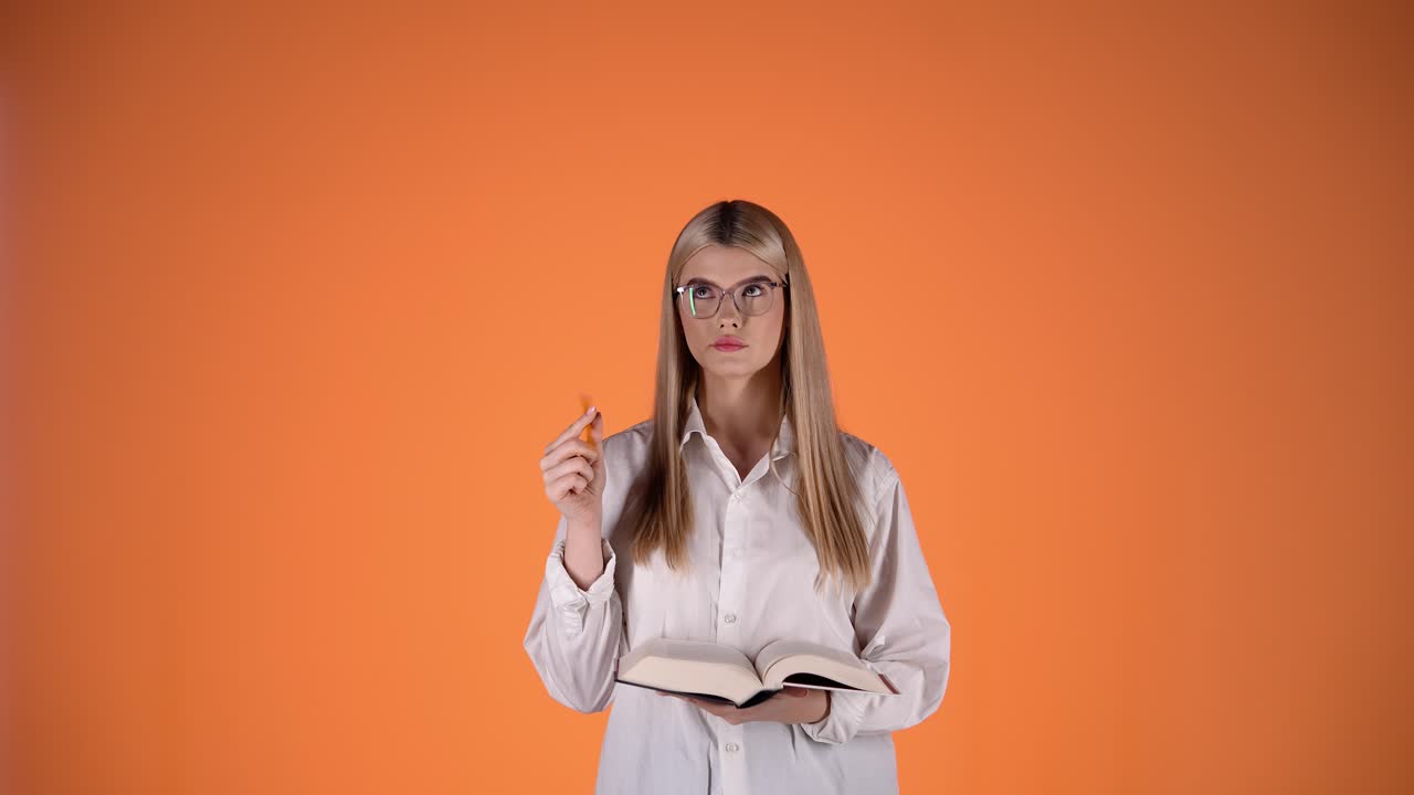 joven rubia pensativa, con lápiz y libro en la mano, colorida fotografía de estudio