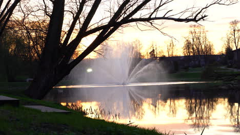 Focus-pull-of-Lake-at-Sunset-with-Water-Fountain-and-Tree-Silhouettes