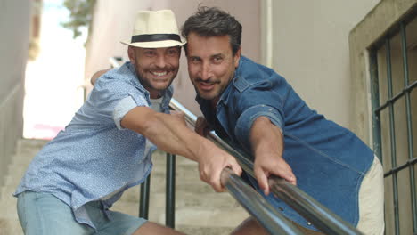Gay-couple-holding-on-to-railing-of-stairs-and-posing