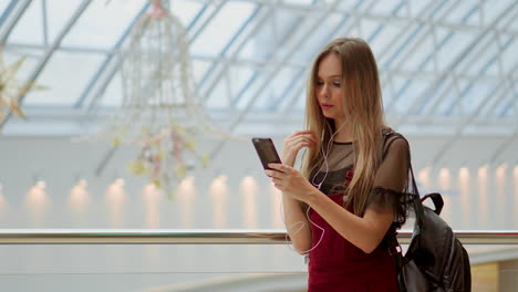 Portrait-of-cheerful-teen-girl-enjoying-music-in-stereo-accessory-connected-to-smartphone-entertaining-on-coffee-break,-smiling-woman-listening-radio-broadcast-via-app-on-cellular-sitting-in-cafe