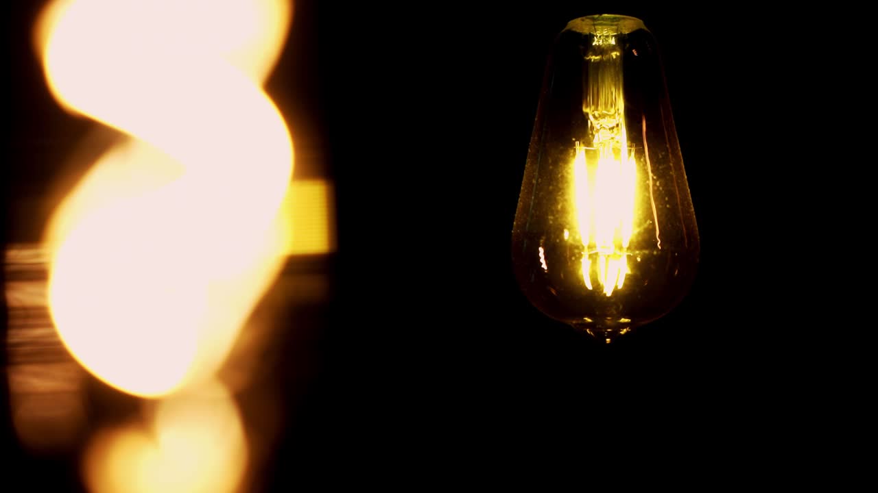 Two vintage edison light bulbs in a dark room, one in focus, one blurred, pan movement