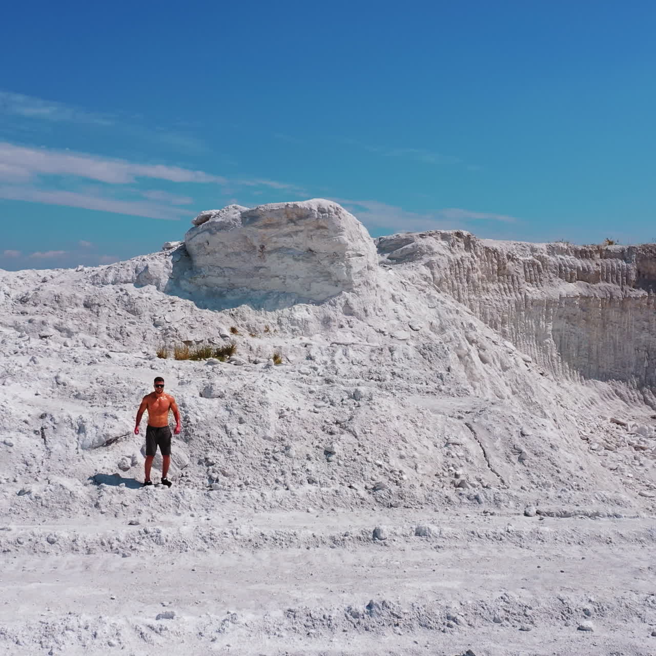 Aerial view on white canyon and a sportsman outdoors. Young athlete walking on beautiful white hill on the natural background in summer. Shirtless athlete in shorts under blue sky.