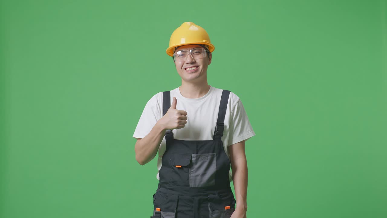Asian Man Worker Wearing Goggles And Safety Helmet Smiling And Showing Thumbs Up Gesture While Standing In The Green Screen Background Studio