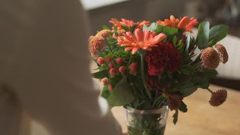 putting vase with orange flowers on wooden table by female hands, slow motion