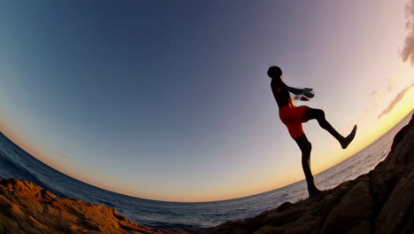 man silhouetted against sunset sky jumps into ocean from rocks