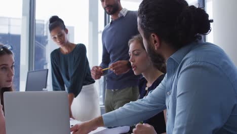 Diverse-group-of-male-and-female-creative-colleagues-gathered-at-a-table-with-laptop-in-discussion