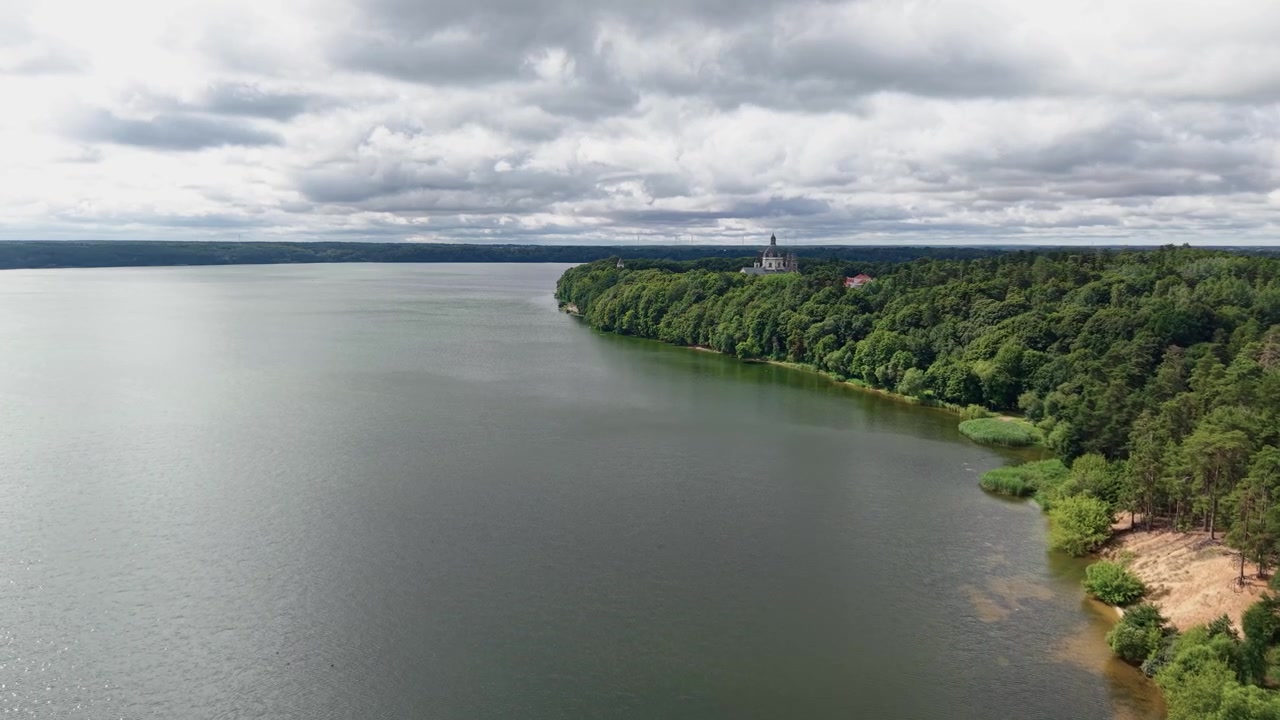 Maestoso video con drone del Monastero di Pažaislis arroccato sopra la Laguna di Kaunas, circondato da una fitta foresta verde e nuvole drammatiche. Ampie riprese aeree panoramiche evidenziano la bellezza naturale e le acque calme.