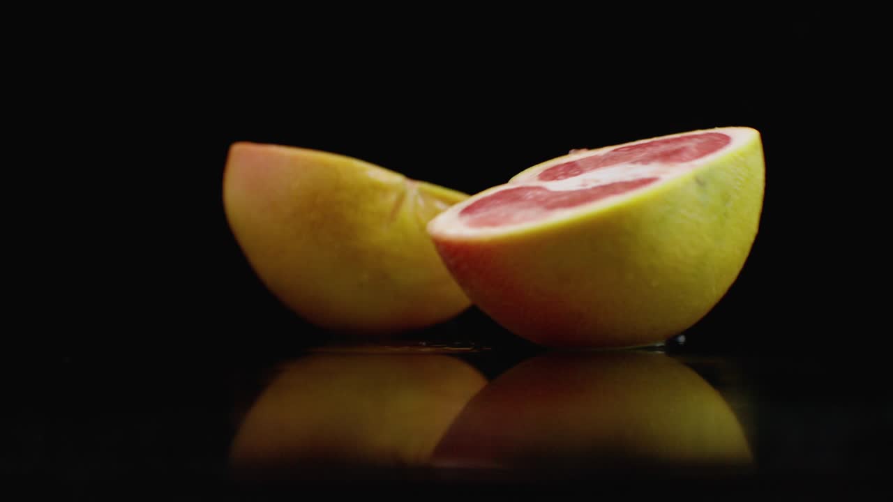 Slow motion. juicy grapefruit with drops and breaks into 2 parts with splashes on a glass table with reflection on a dark background
