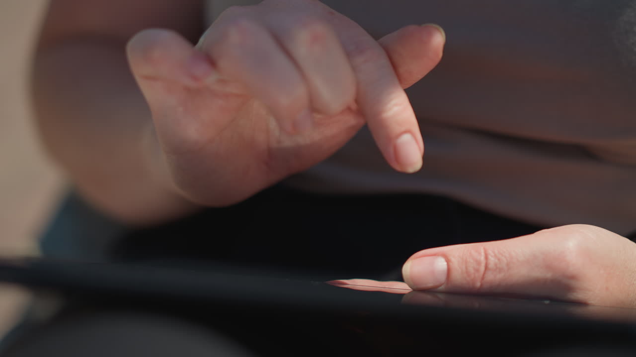 Close up of tech savvy person sliding through tablet outdoors under warm sunlight, showing gentle motion and reflection, symbolizing focus, innovation, digital creativity