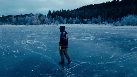 indre fosen, trondelag county, norway - a man strolling on the snow-covered surface of omundvatnet, encircled by coniferous trees, with a mountain in the background - tracking shot