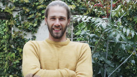 Portrait-of-happy-caucasian-man-wearing-yellow-jumper-crossing-arms-in-garden,-slow-motion