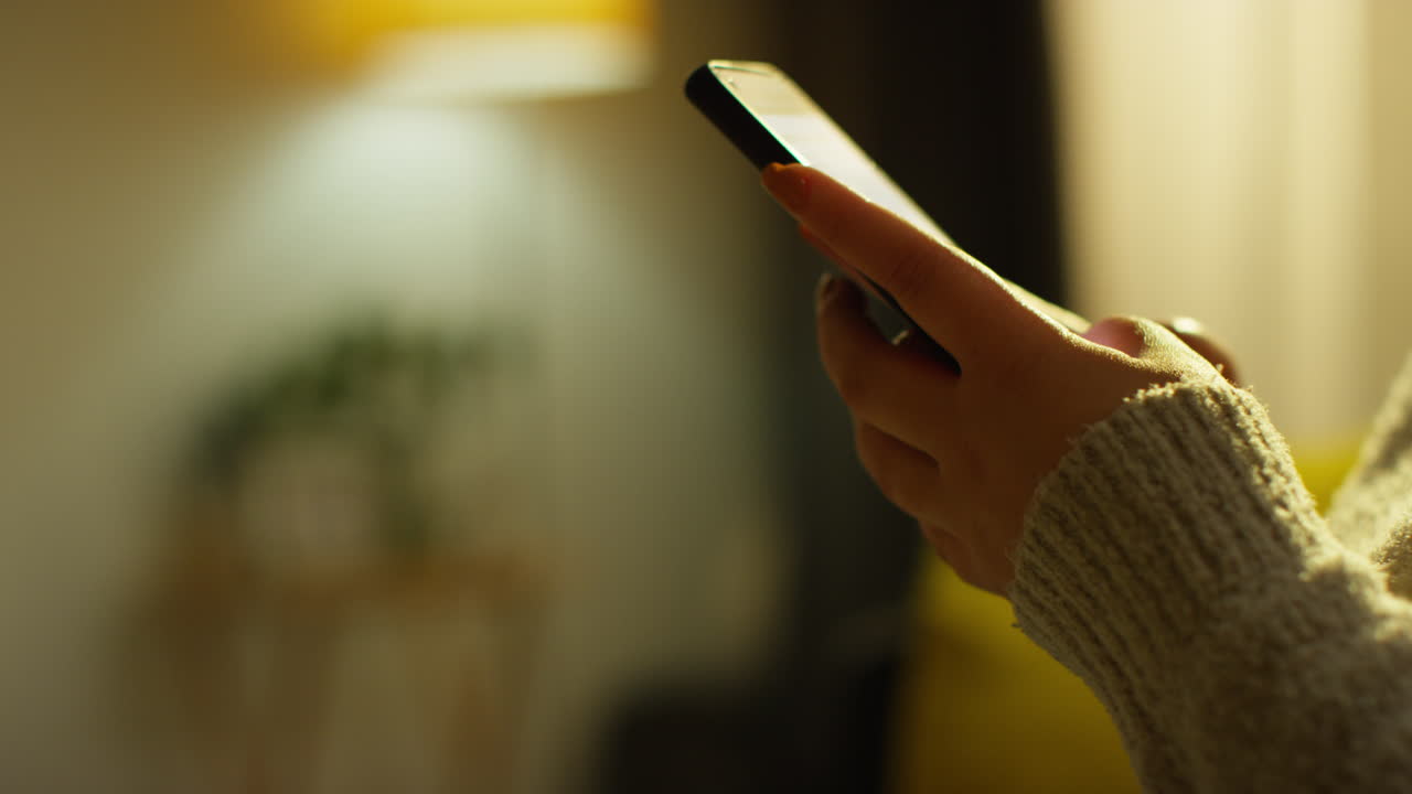 cerca de las manos de una mujer que pasa la noche en casa sentada en el sofá con el teléfono móvil desplazándose por internet o las redes sociales