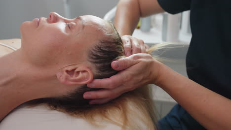 skin therapist tilts head of relaxed client lying on treatment bed with soothing hands providing neck support and gentle facial stretch in professional spa environment for maximum comfort
