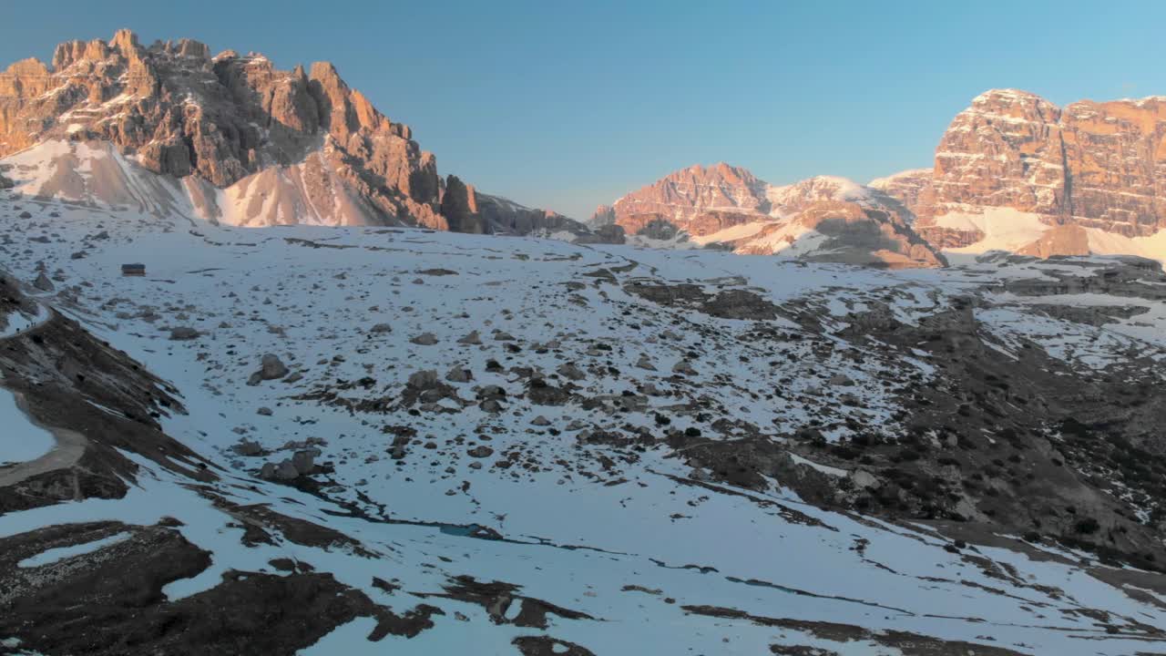 4K drone footage panning across the snowy Dolomites at sunset, capturing dramatic peaks and warm golden hour light in a stunning alpine landscape.