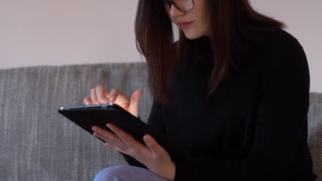 tilting up medium shot of a woman sitting on couch, using tablet