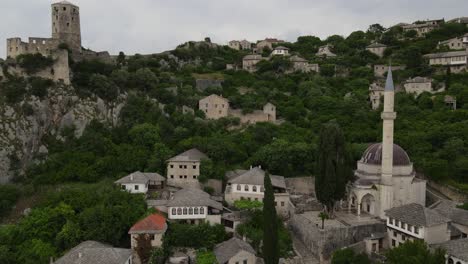 Drohnenansicht-Der-Historischen-Bosnischen-Stadt-Am-Ufer-Des-Flusses-Neretva,-Der-Burg-Der-Beliebten-Bosnischen-Stadt-Pocitelj-Mit-Ihren-Steingebäuden-Und-Der-Grünen-Landschaft