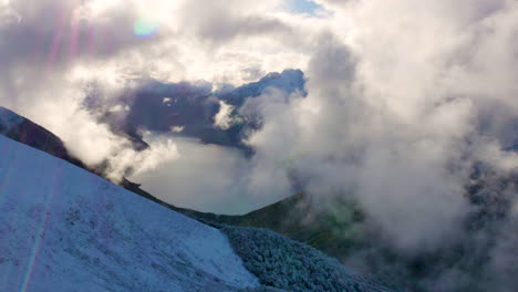 aerial top down of snowy mountains showing flying clouds and calm lake in the valley of fiordland national park in new zealand