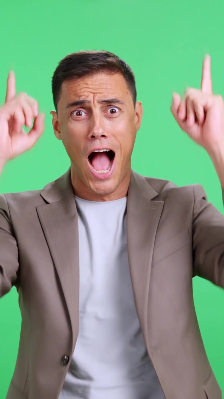 Surprised man pointing up with amazement on green screen