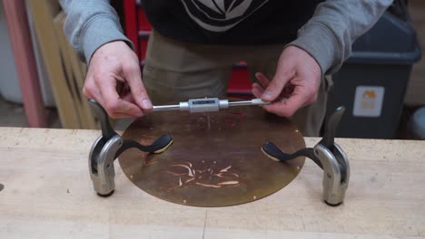 guitar build - craftsman's hands tapping a hole in copper guitar's cover plate at the work bench