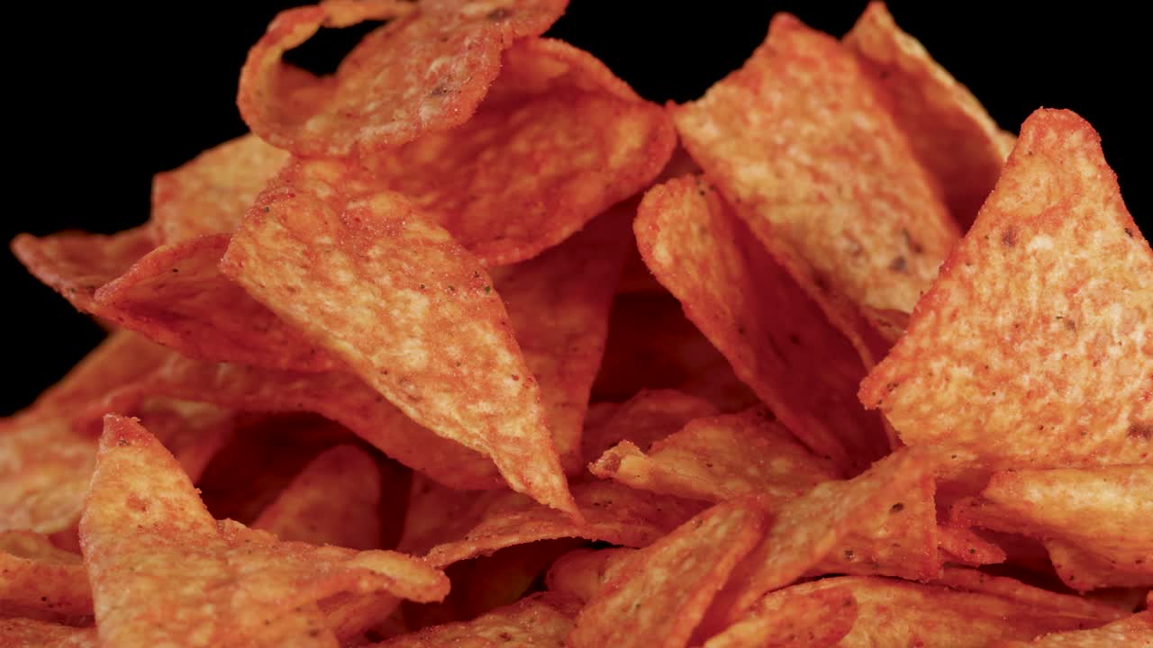 Nachos triangolari che cadono a rallentatore su uno sfondo nero, l'illuminazione nitida mette in risalto la texture