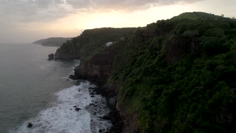Aerial-shot-of-ocean-waves-crashing-coastline-cliff-suring-sunset,-El-Zonte-beach-,-La-Libertad,-El-Salvador