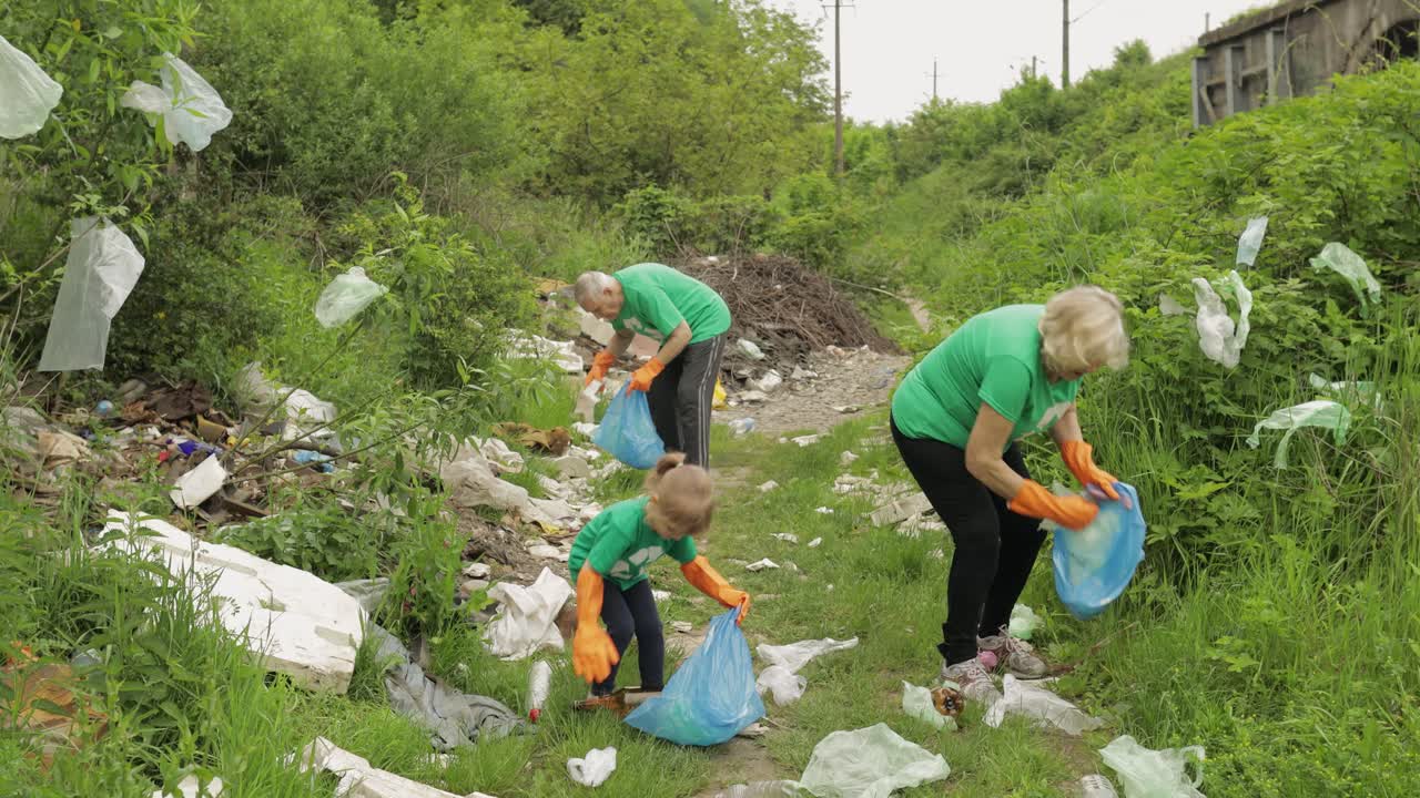 Team of nature activists in eco T-shirts picking up plastic trash in park. Recycle, earth pollution