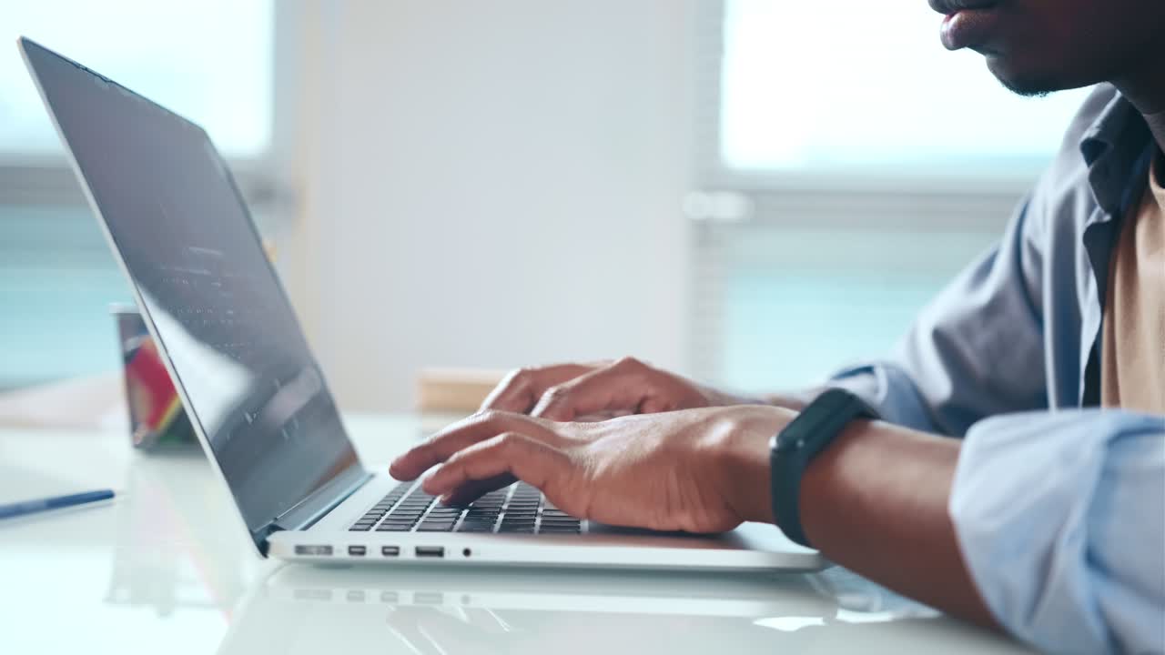 vista de cerca de las manos del usuario afroamericano masculino escribiendo en el teclado de la computadora portátil