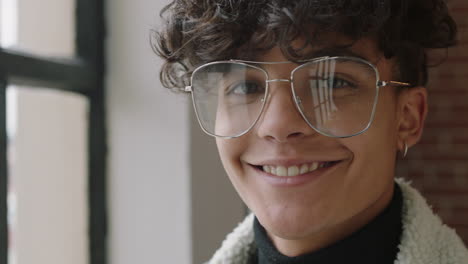 close up portrait stylish young hispanic man student smiling happy enjoying successful lifestyle wearing trendy fashion glasses looking out window in modern apartment loft