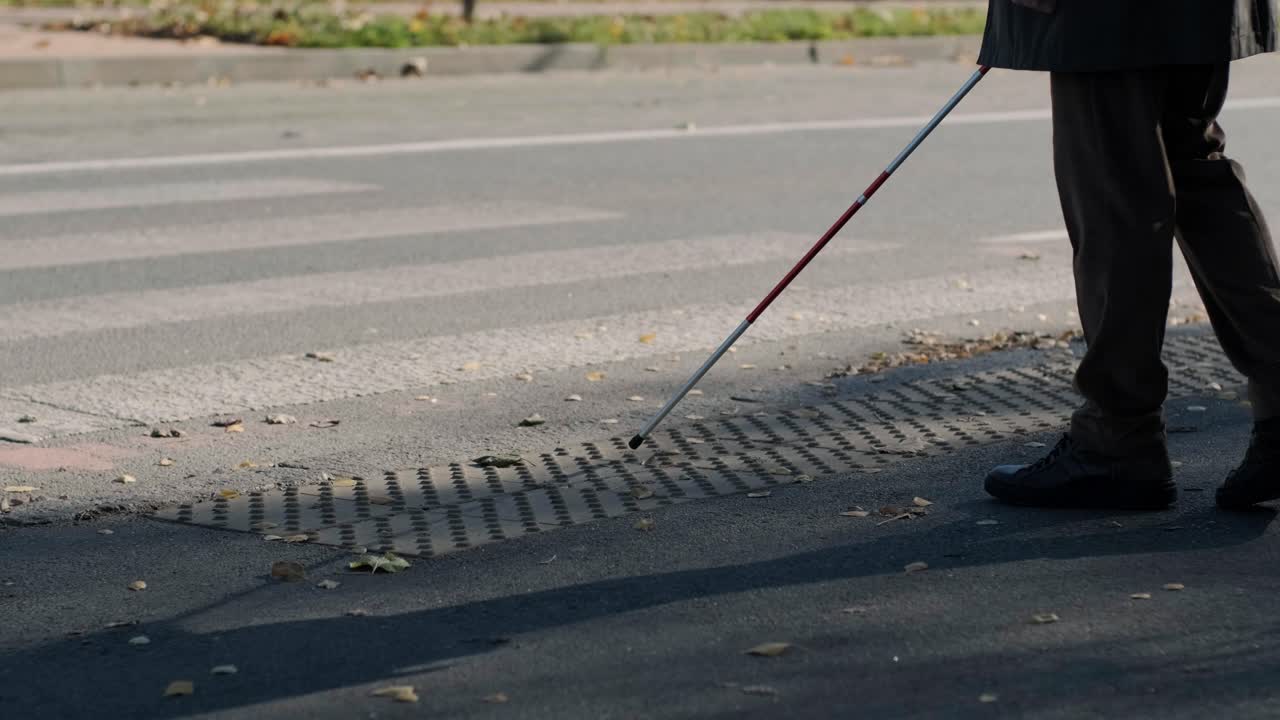 시각장애인 남자가 자신의 지이로 도로를 건너고 있는 모습이 도시에서 시각장애인을 위한 촉각적인 보행자 보행자 도로의 도움으로 보여진다.