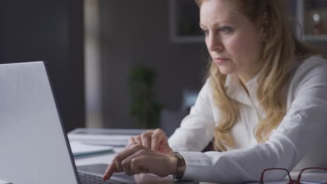 una mujer de negocios madura y profesional sentada en su escritorio usando una computadora portátil.