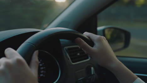 woman driver hands on steering wheel driving car in city on the road at rush hour travelling to destination at sunset