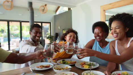 multi-generation family around table at home doing cheers with water towards camera
