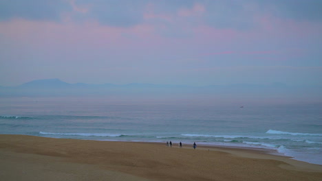 Filmischer-Früher-Morgen,-Rosa,-Violetter-Sonnenuntergang,-Sonnenaufgang,-Surfer,-Die-Aus-Der-Ferne-Am-Strand,-Berg,-Küstenlandschaft,-Hoosegor-Seignosse,-Biarritz,-Baskenland,-Spanien,-Frankreich,-WSL,-Riesige-Wellen,-Wellengang,-Brandung-Laufen