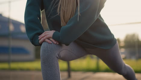 primer plano de atleta con suéter verde con la mano en la rodilla, el cabello fluyendo hacia abajo mientras participa en una sesión de fitness al aire libre, haciendo hincapié en el enfoque en el ejercicio y la aptitud física durante la rutina de entrenamiento