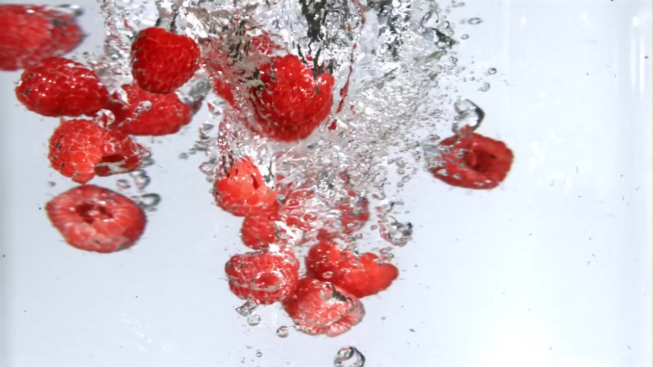Fresh Red Raspberries Splashing and Falling into Clear Water