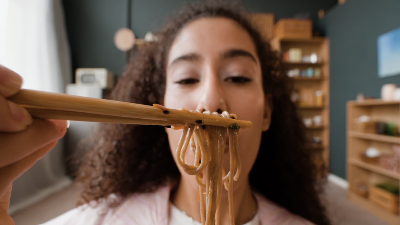 una mujer comiendo fideos con palillos