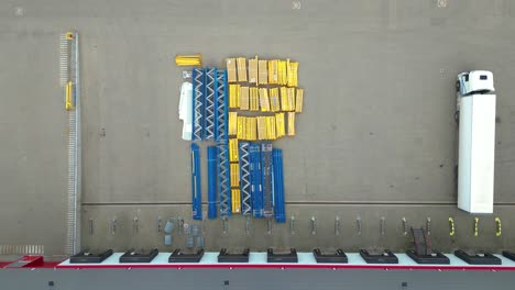 Aerial-view-of-a-semi-trucks-with-cargo-trailers-standing-on-warehouses-ramps-for-loading-unloading-goods-on-the-big-logistics-park-with-loading-hub