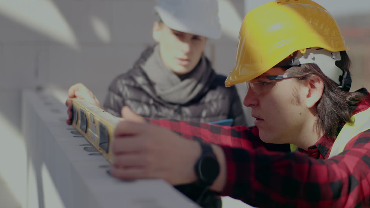Confident young male worker analyzing wall with level by female engineer discussing at construction site