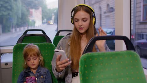 child girl with mother using smartphone with headphones, earphones listening music, funny dancing