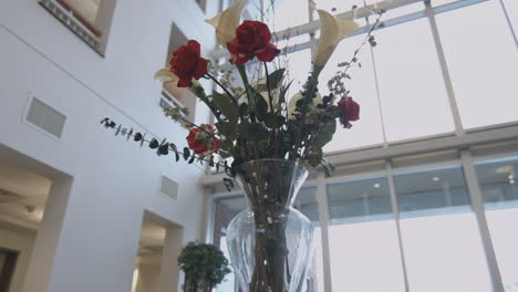 a glass vase filled with a bouquet of flowers red roses and white lilies in a bright airy atrium slider shot