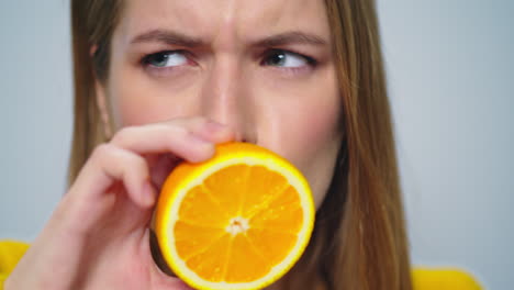 closeup positive woman making funny faces with orange in hands in studio.