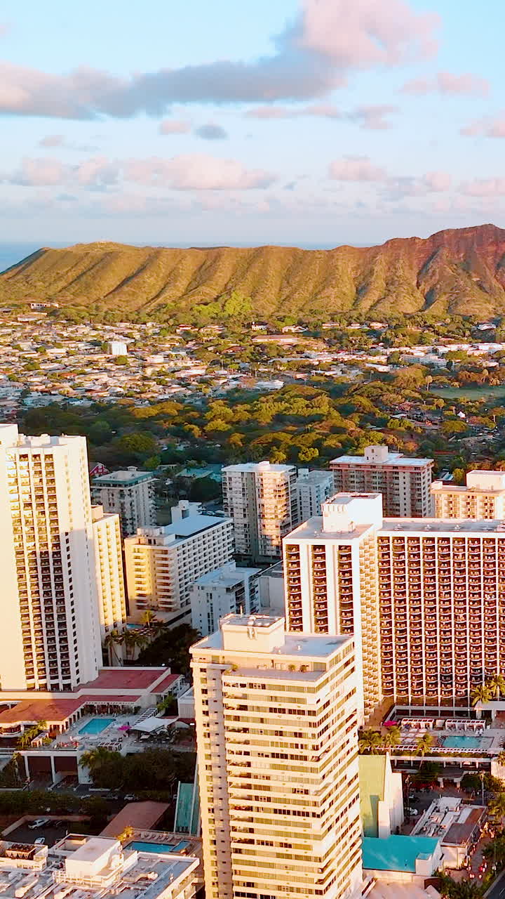 Edifici urbani e hotel a Waikiki durante l'ora d'oro con un cratere vulcanico e l'Oceano Pacifico. Vista aerea del paesaggio urbano di Honolulu con il cratere Diamond Head sullo sfondo. Video verticale